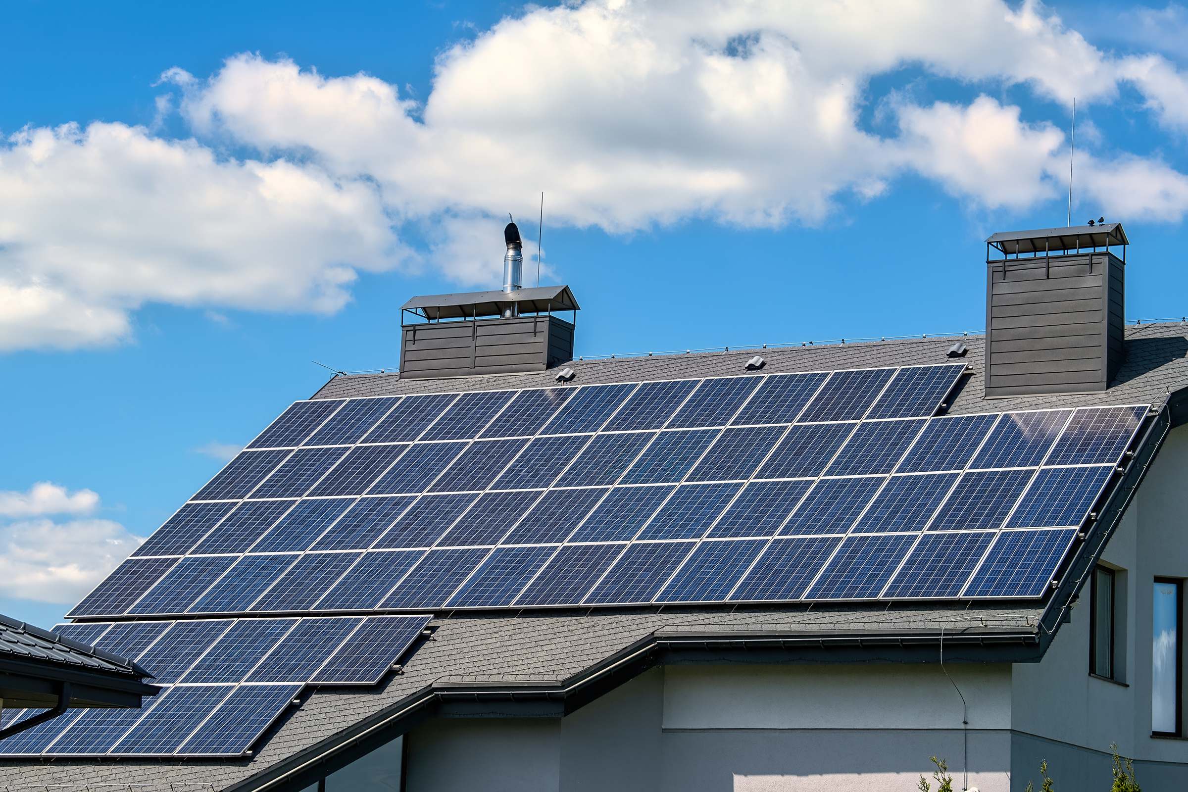 Rows of dark solar panels on a gray shingle roof under a blue sky